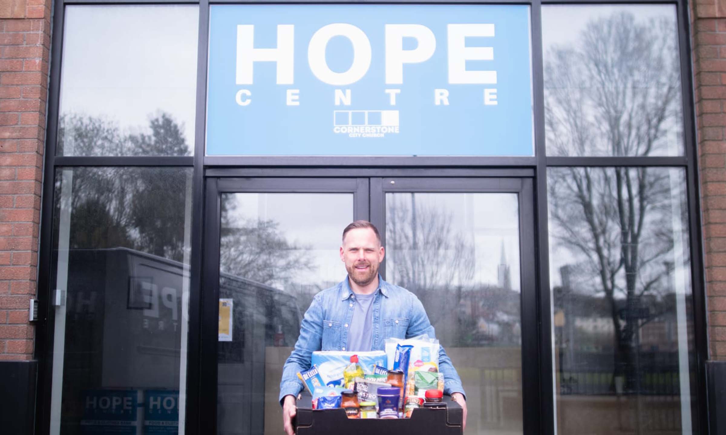 Man with box of shopping stood at entrance to Hope Centre
