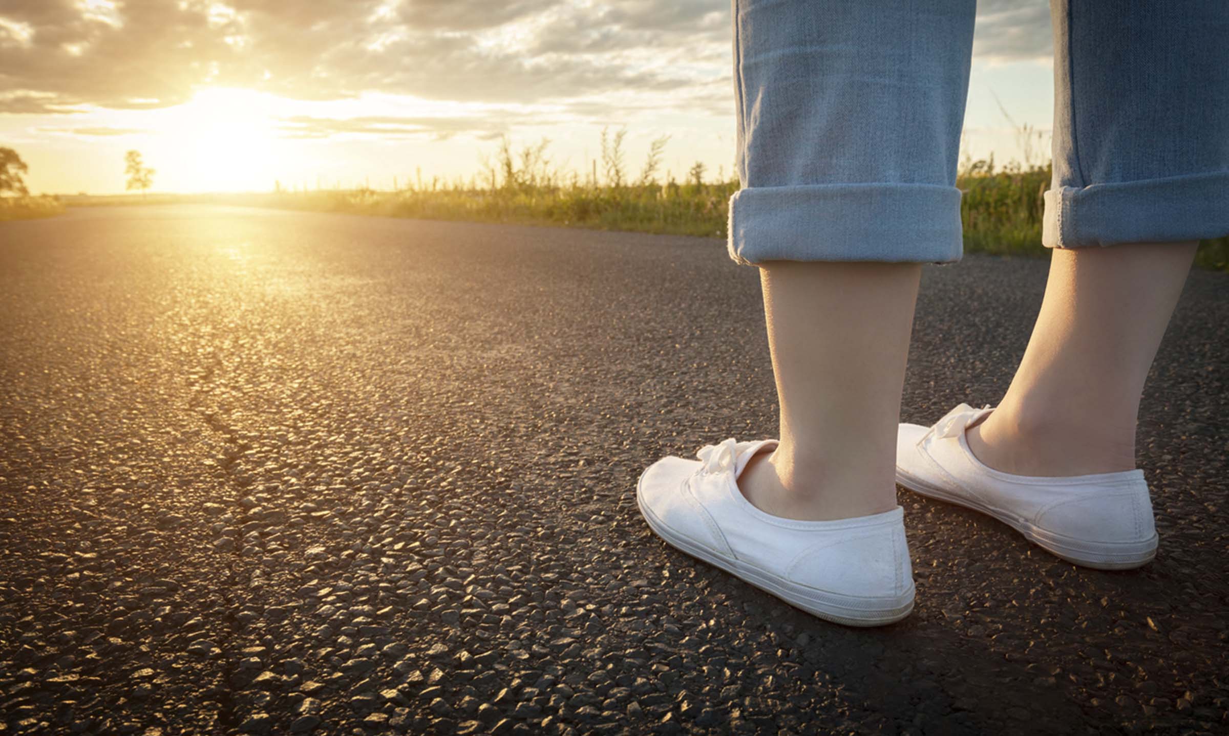 Woman's legs in jeans and plimsols stood on an empty road